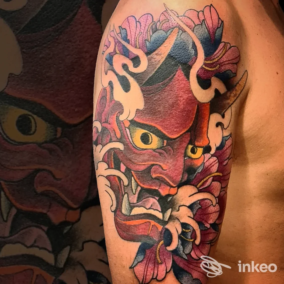 Grande tatuaggio colorato a tema maschera oni con fiori sul braccio superiore. Love Hate Tattoo Studio, Marina di Carrara.