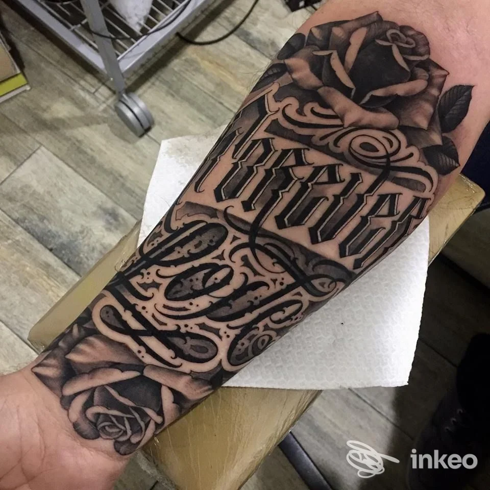 Ampio tatuaggio in bianco e nero su avambraccio con rose e lettering ornamentale. Luxury Tattoo, Grosseto.