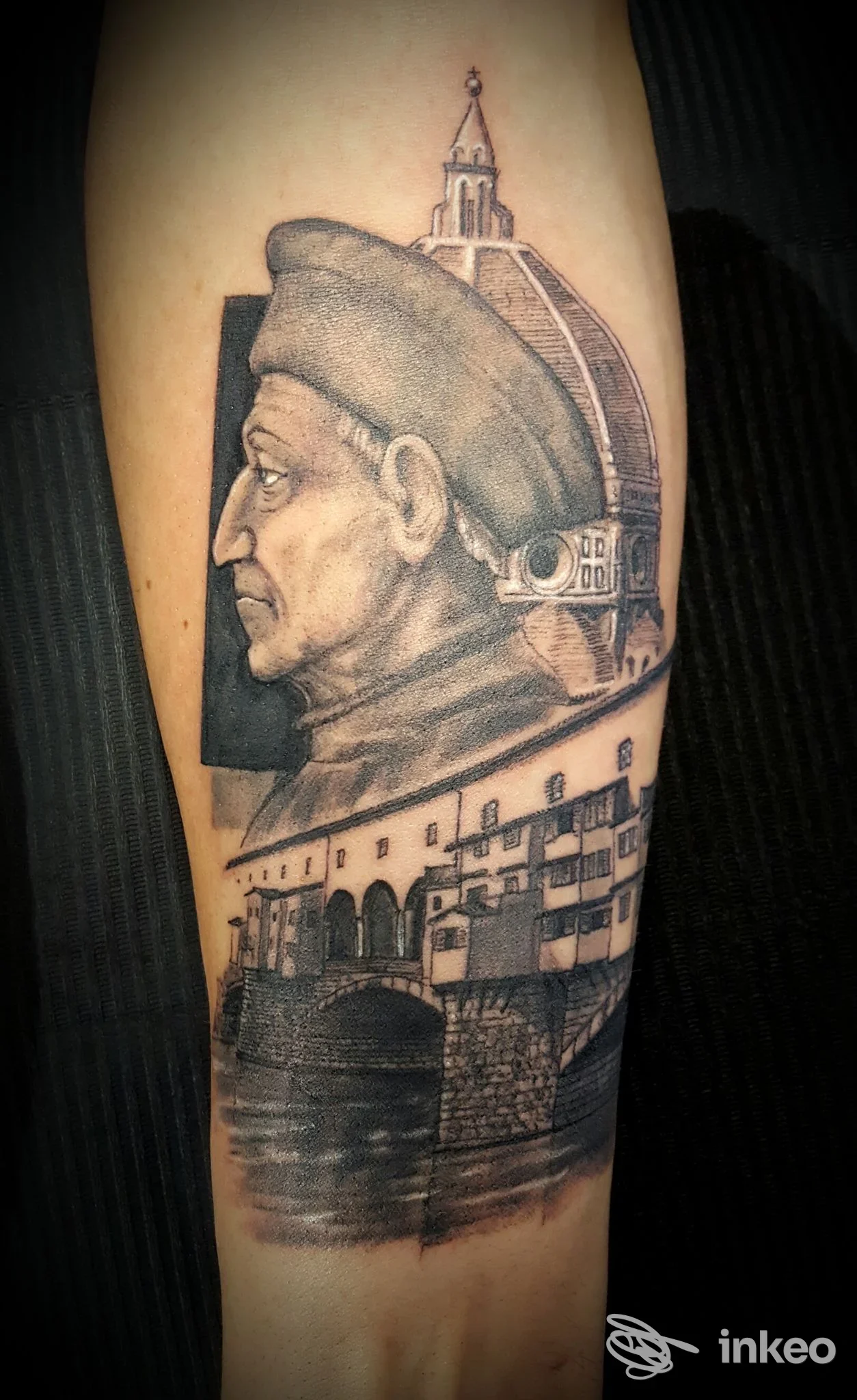 Tatuaggio realistico in bianco e nero sull'avambraccio con ritratto in profilo e veduta architettonica, scattato da Nexus Tattoo a Montespertoli.