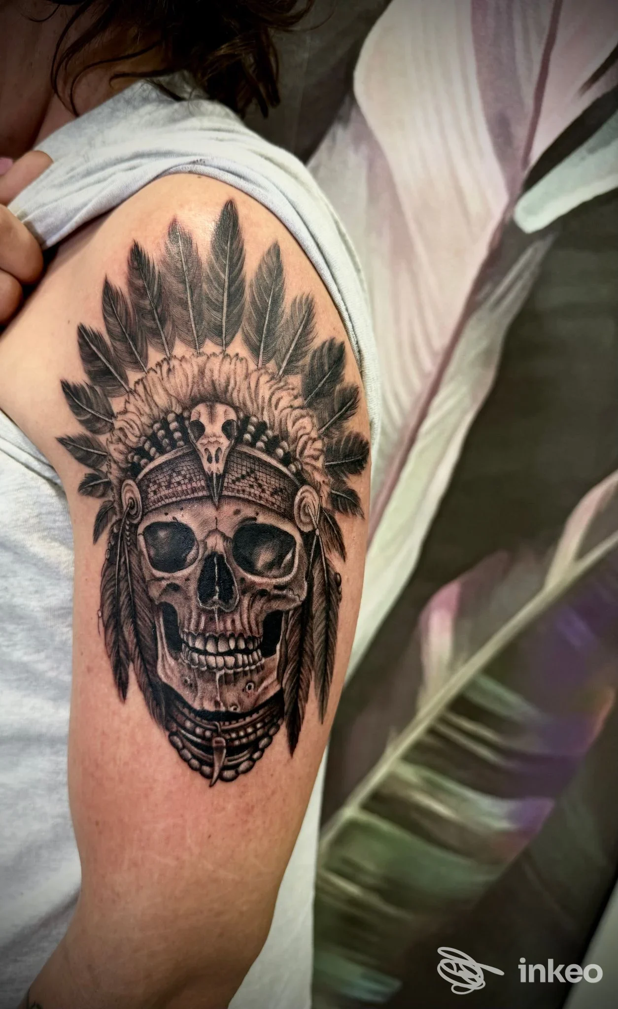 Tatuaggio in bianco e nero di teschio con copricapo piumato sul braccio. Musa Tattoo Studio, Pietrasanta.