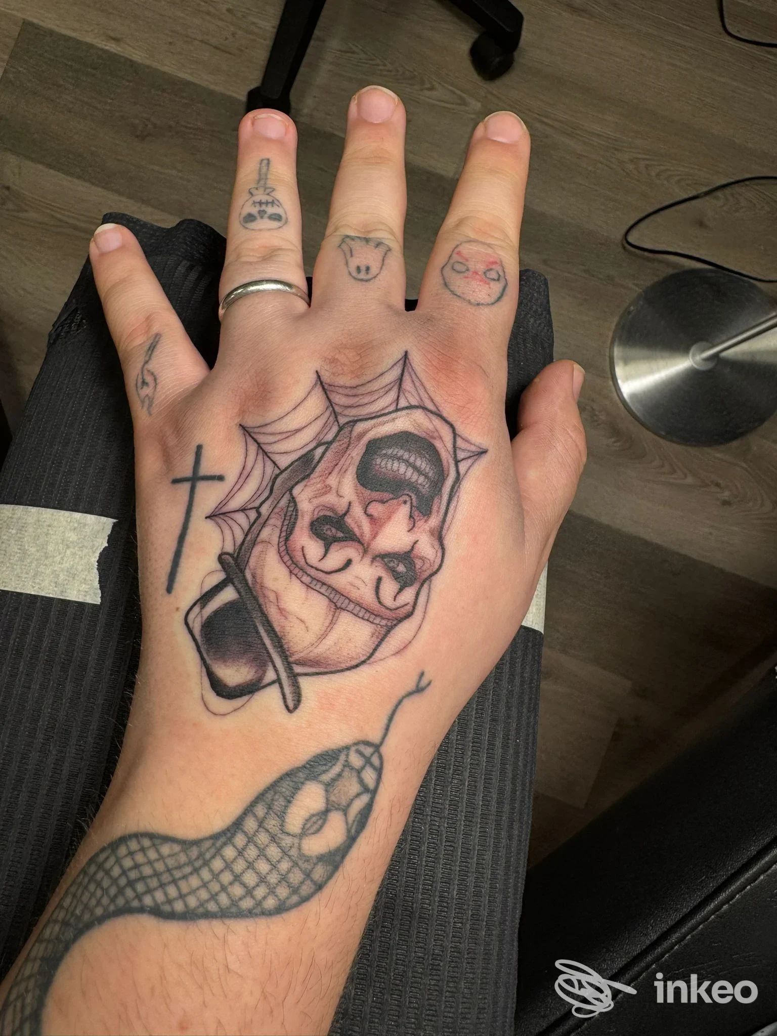 Primo piano del dorso di una mano tatuata con volto grottesco, serpente e simboli; foto inviata da Pink Tattoo Studio, Arezzo.