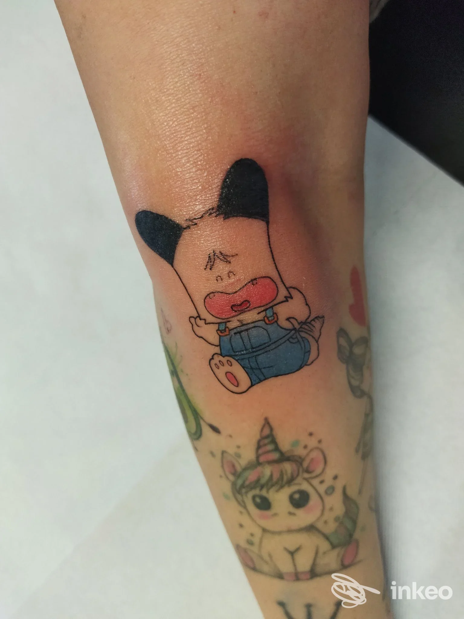 Avambraccio con due tatuaggi cartoon colorati: un personaggio rosa con orecchie nere e un unicorno. Sisters Tattoo & Piercing, Fornaci di Barga.