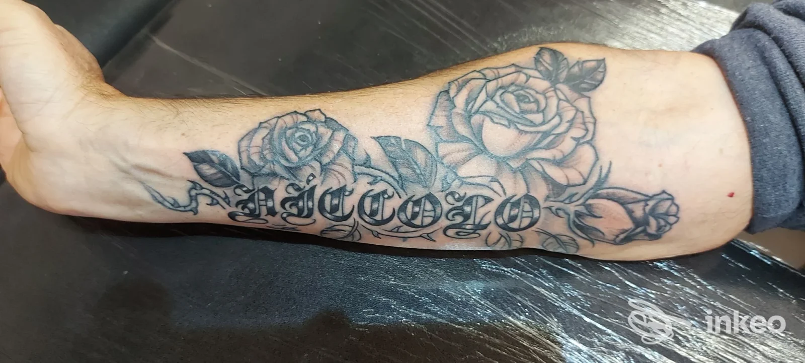 Avambraccio tatuato con rose in nero/grigio e scritta ornamentale, foto fornita da Tattoo studio anna vannetti a Grassina.