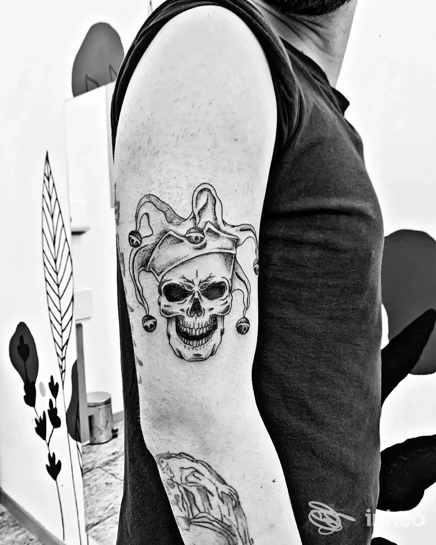 Tatuaggio black & grey di un teschio con cappello da giullare sul braccio superiore, foto di Zizzi Loft Tattoo Studio ad Arezzo.