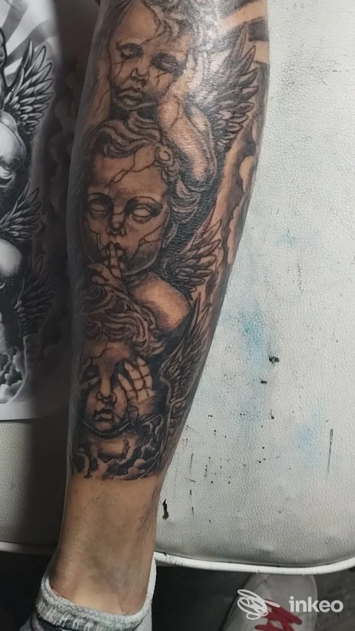 Tatuaggio in bianco e nero sul polpaccio con volti e ali, foto fornita da Alpha Omega Tattoo, Trento.