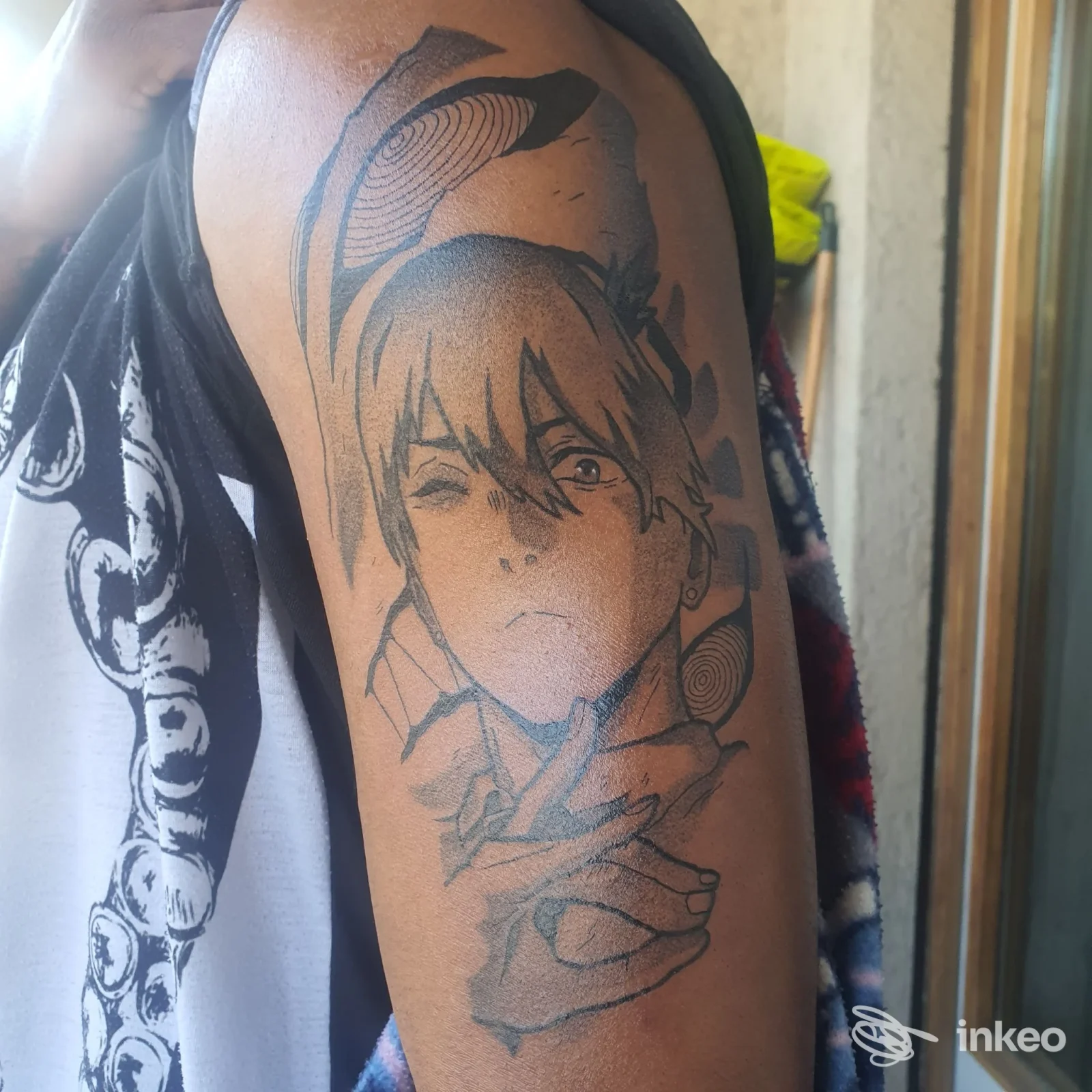 Tatuaggio in nero su braccio: volto stilizzato e mano, fotografato all'altezza della spalla. Anthracite Tattoo Studio, Trento.