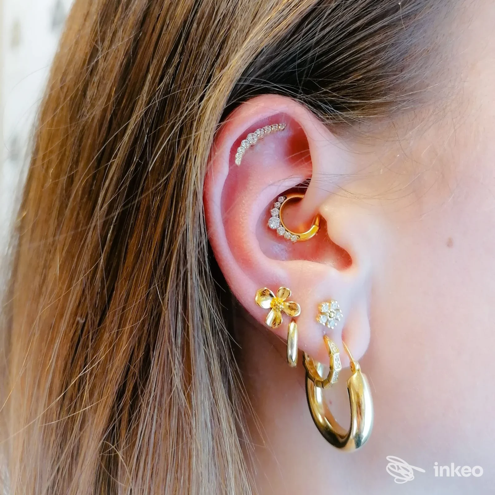 Primo piano di un orecchio con più piercing dorati e brillanti, foto per Astrid Body Piercing Studio, Bolzano.