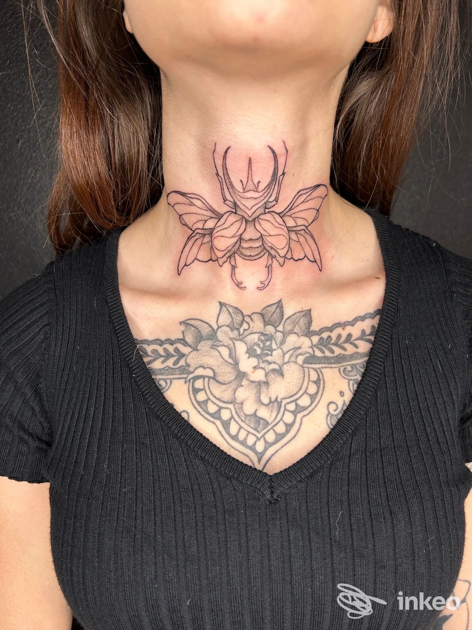 Tatuaggio a linee di un insetto sul collo sopra un pettorale floreale, realizzato da Bootleg Art Tattoo a Riva del Garda.