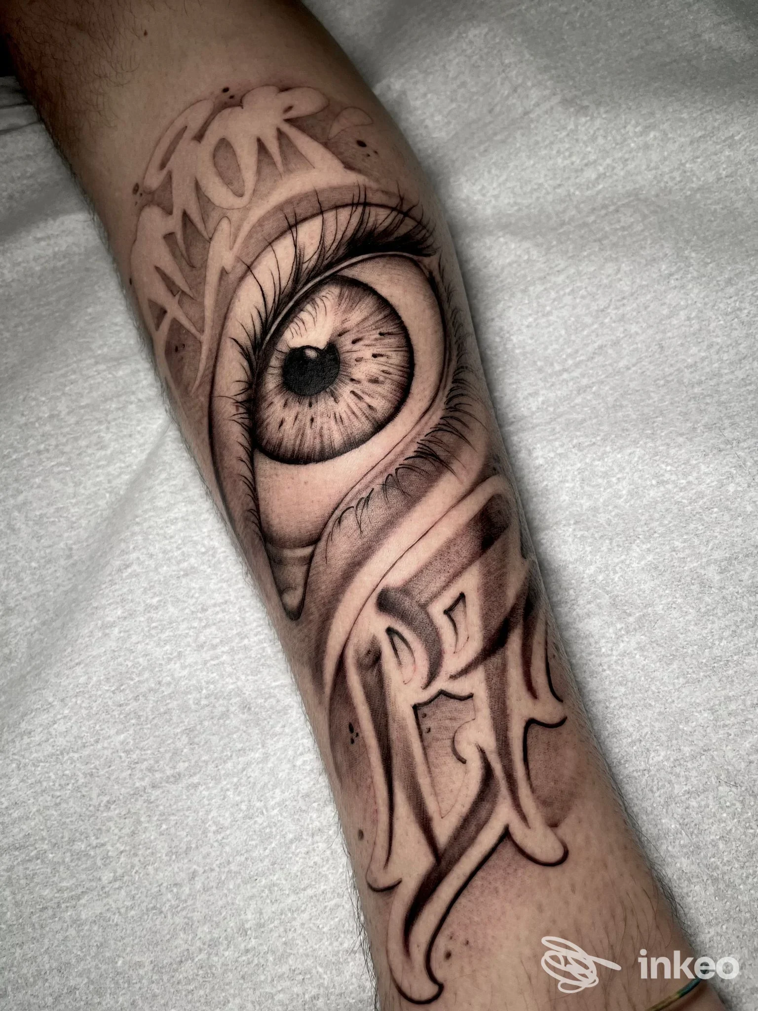 Tatuaggio realistico di un occhio su avambraccio, con lettere decorative; immagine fornita da Bronx Tattoo a Riva del Garda.