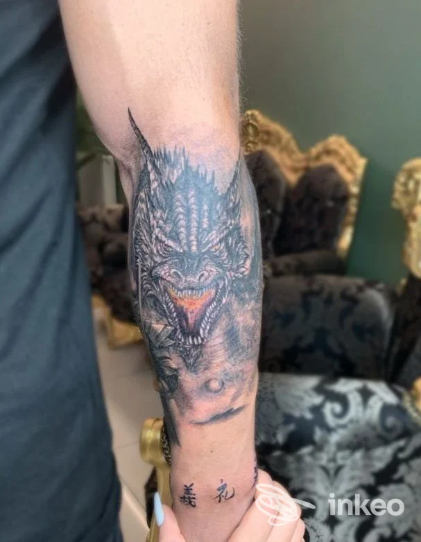 Avambraccio tatuato con grande dragone realistico e piccoli caratteri vicino al polso, Divine Tattoo, Runggaditsch.