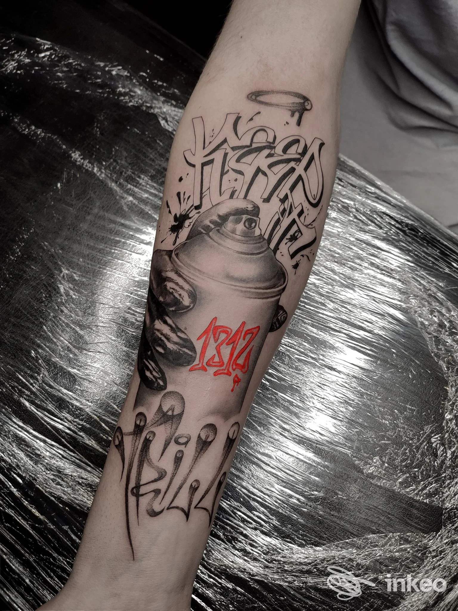 Avambraccio tatuato con bomboletta spray stilizzata, lettering nero e numeri rossi. Foto per El Tatuador Studio, Mezzolombardo.