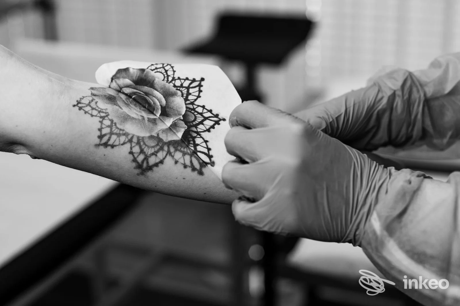 Avambraccio tatuato con rosa e motivo pizzo, operatrice con guanti durante la rifinitura nello studio Endless Tattoo BZ a Bolzano.