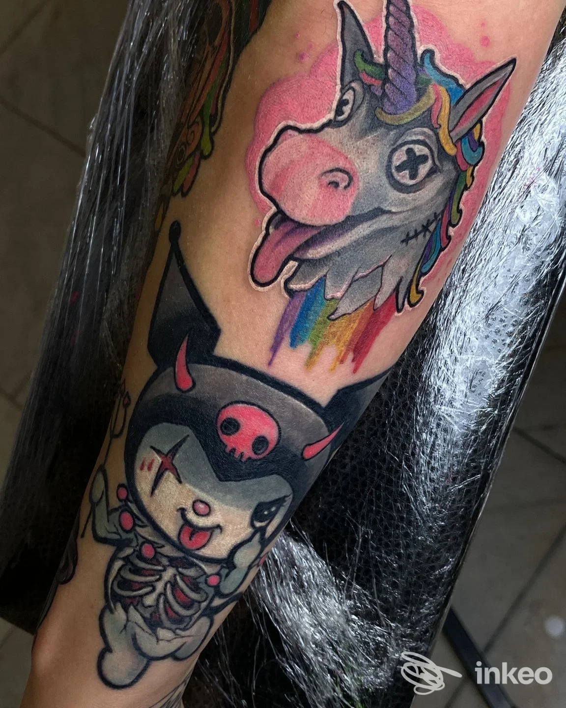 Avambraccio tatuato con unicorno colorato e personaggio scheletrico, foto per Exodus Tattoo e Piercing a Bolzano.