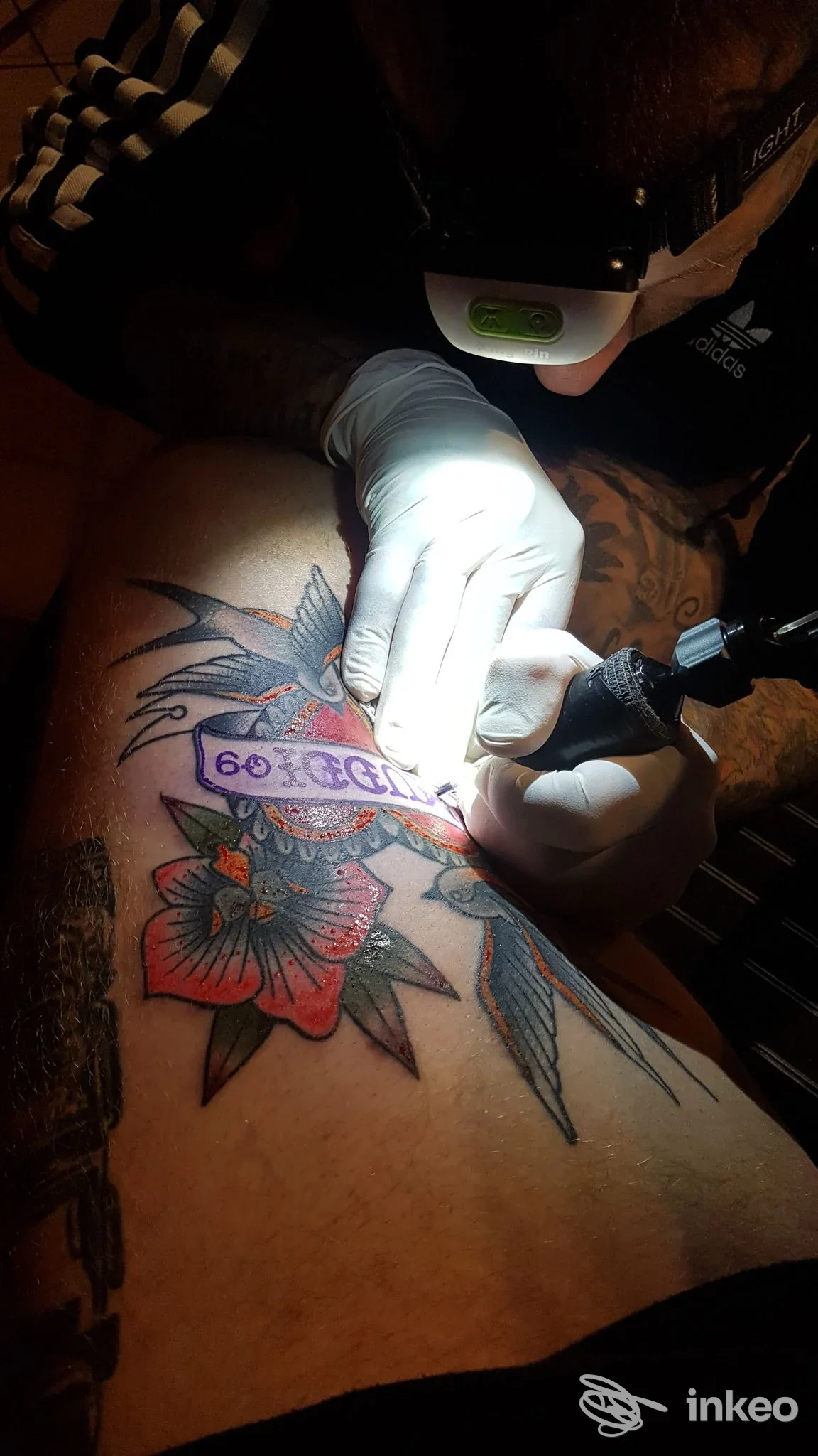 Tatuaggio in corso su coscia con fiori e nastro, fotografato nello studio Für immer mein Tattoo Shop a Vipiteno.