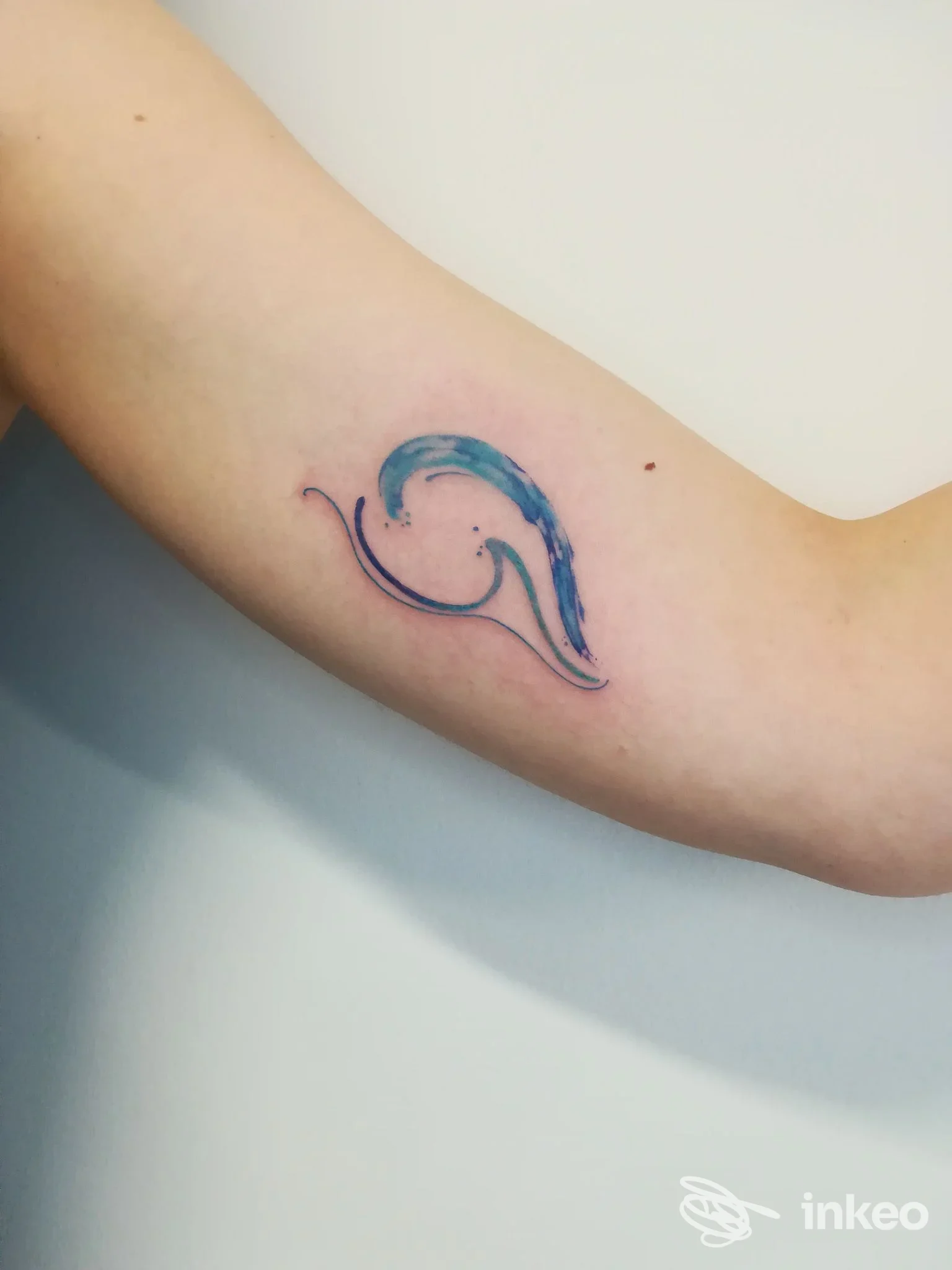 Tatuaggio a onda blu su avambraccio, stile minimale, colori blu e viola, senza testo o elementi di testo visibili.