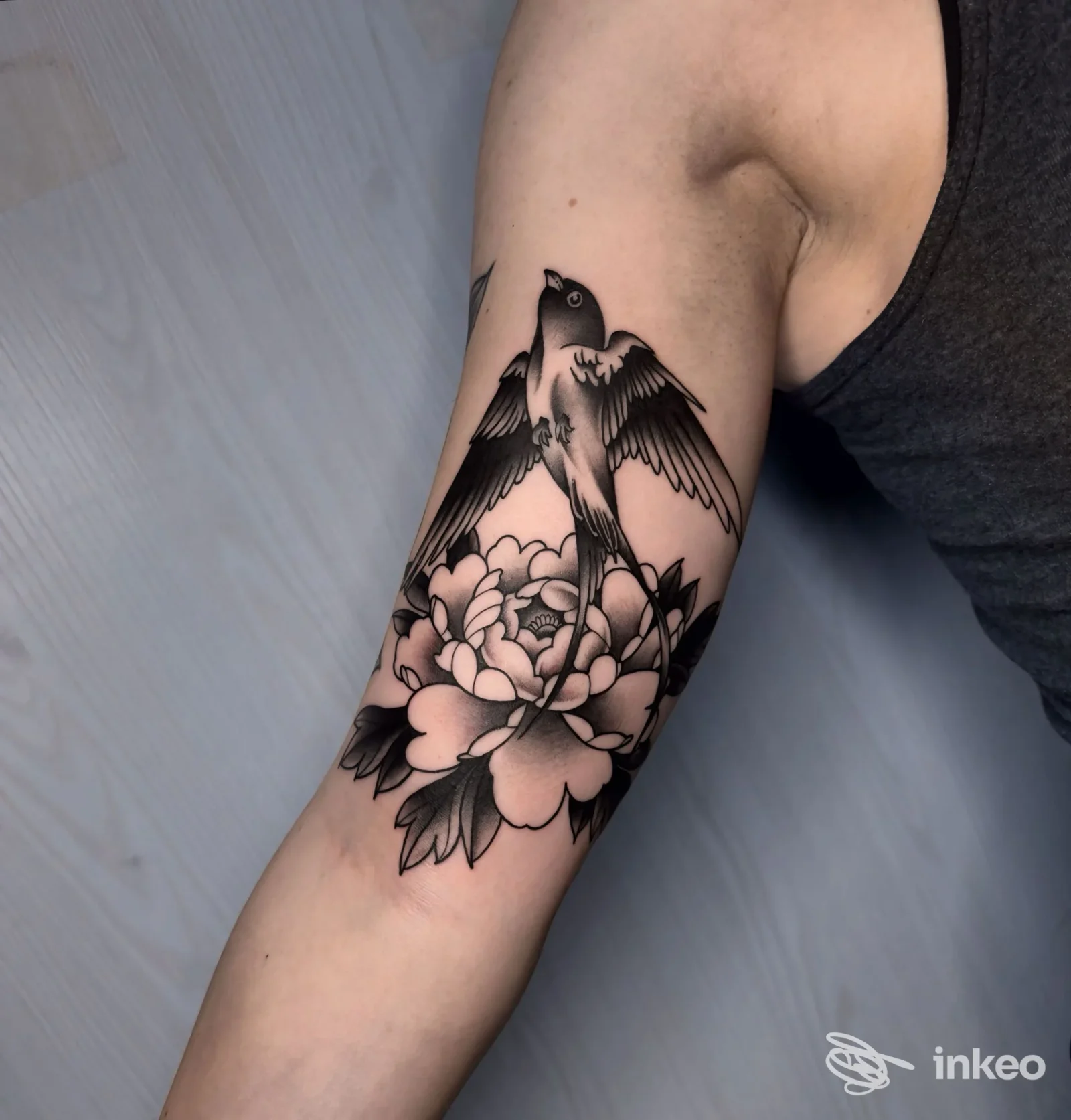 Tatuaggio uccello e fiori sul bicipite realizzato da Inkmate Tattoo Studio a Levico Terme.