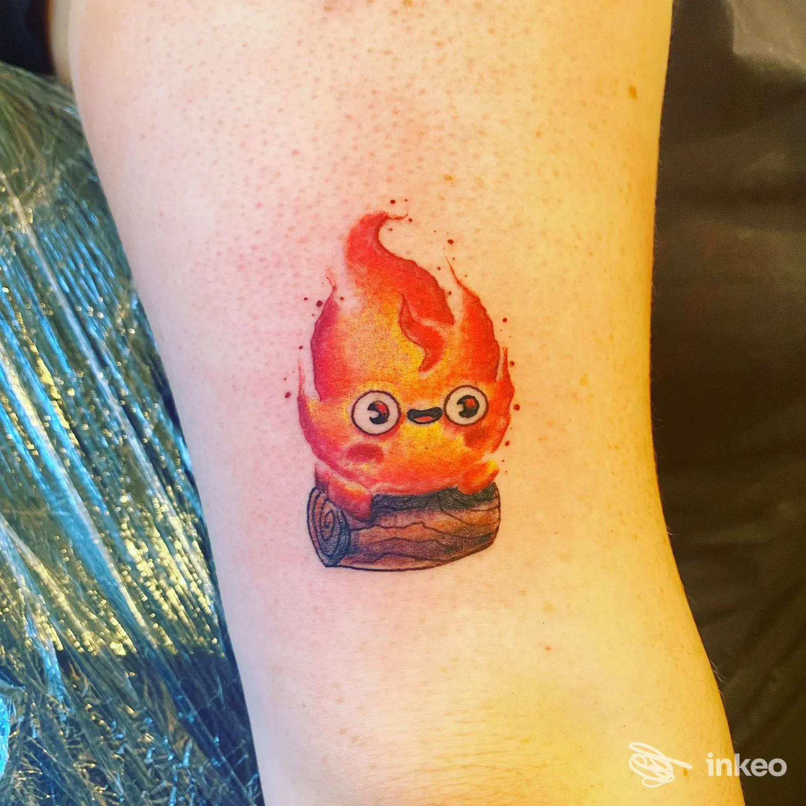 Tatuaggio colorato di una fiamma sorridente su ceppo, avambraccio. Isc Tattoo Di Caruso Salvatore, Rovereto.