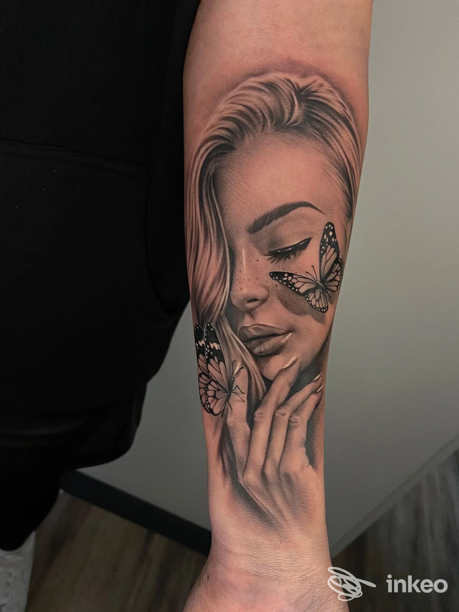 Tatuaggio realistico in bianco e nero su avambraccio con volto femminile e farfalle, Infamous Tattoo, Campo Tures.