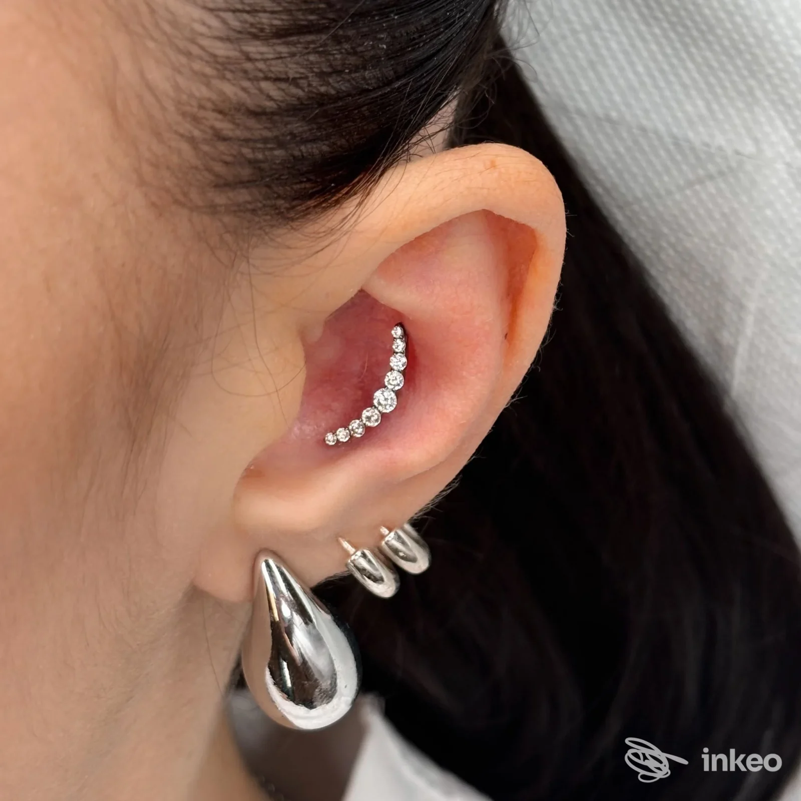 Primo piano di un orecchio con tre piercing e un orecchino a goccia, lavoro effettuato da Lux Tattoo & Piercing Studio a Rovereto.