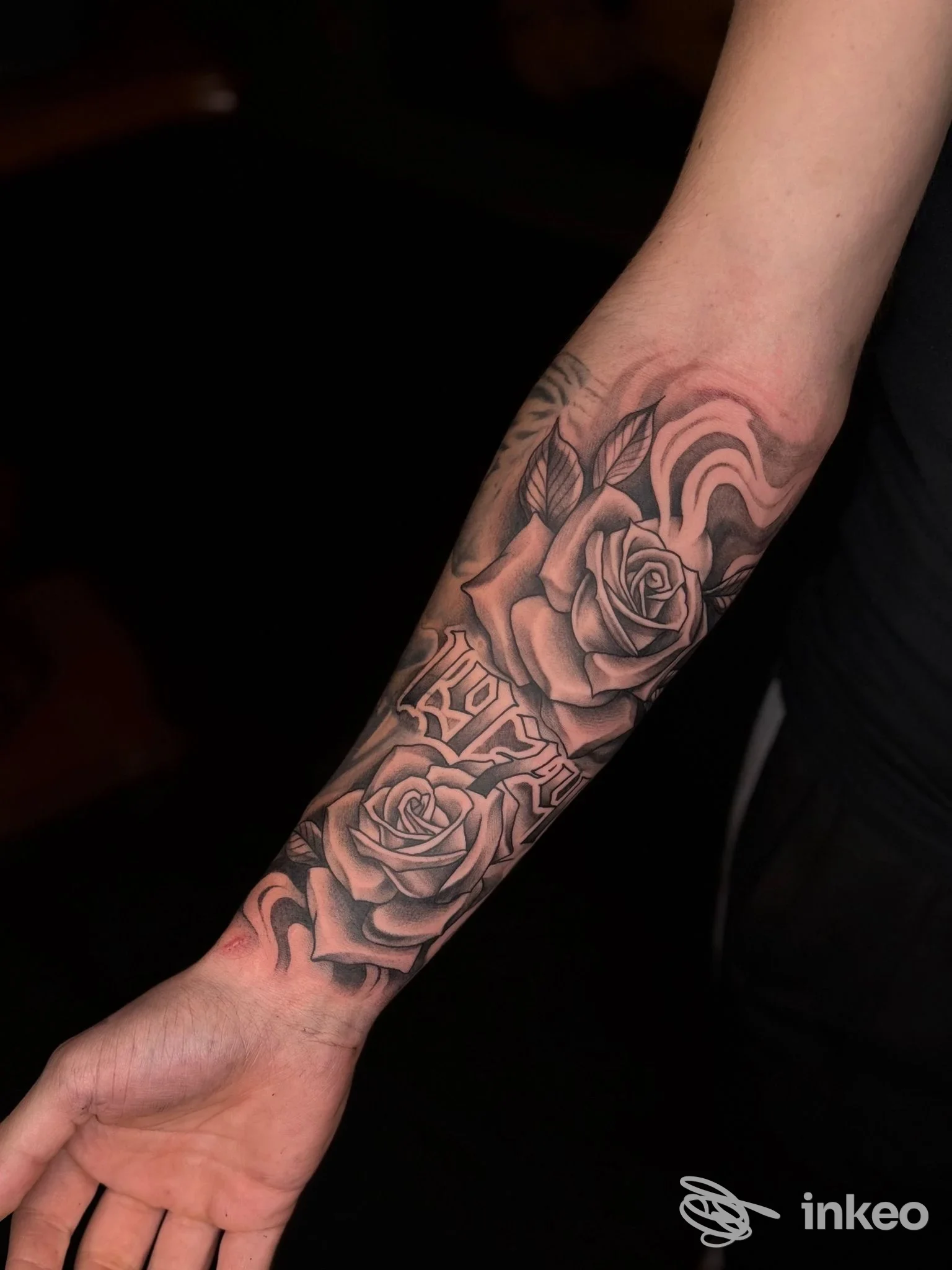 Avambraccio con tatuaggio realistico in bianco e nero raffigurante rose e ornamenti; fotografia in primo piano per Mea Culpa Tattoo Studio, Riva del Garda.