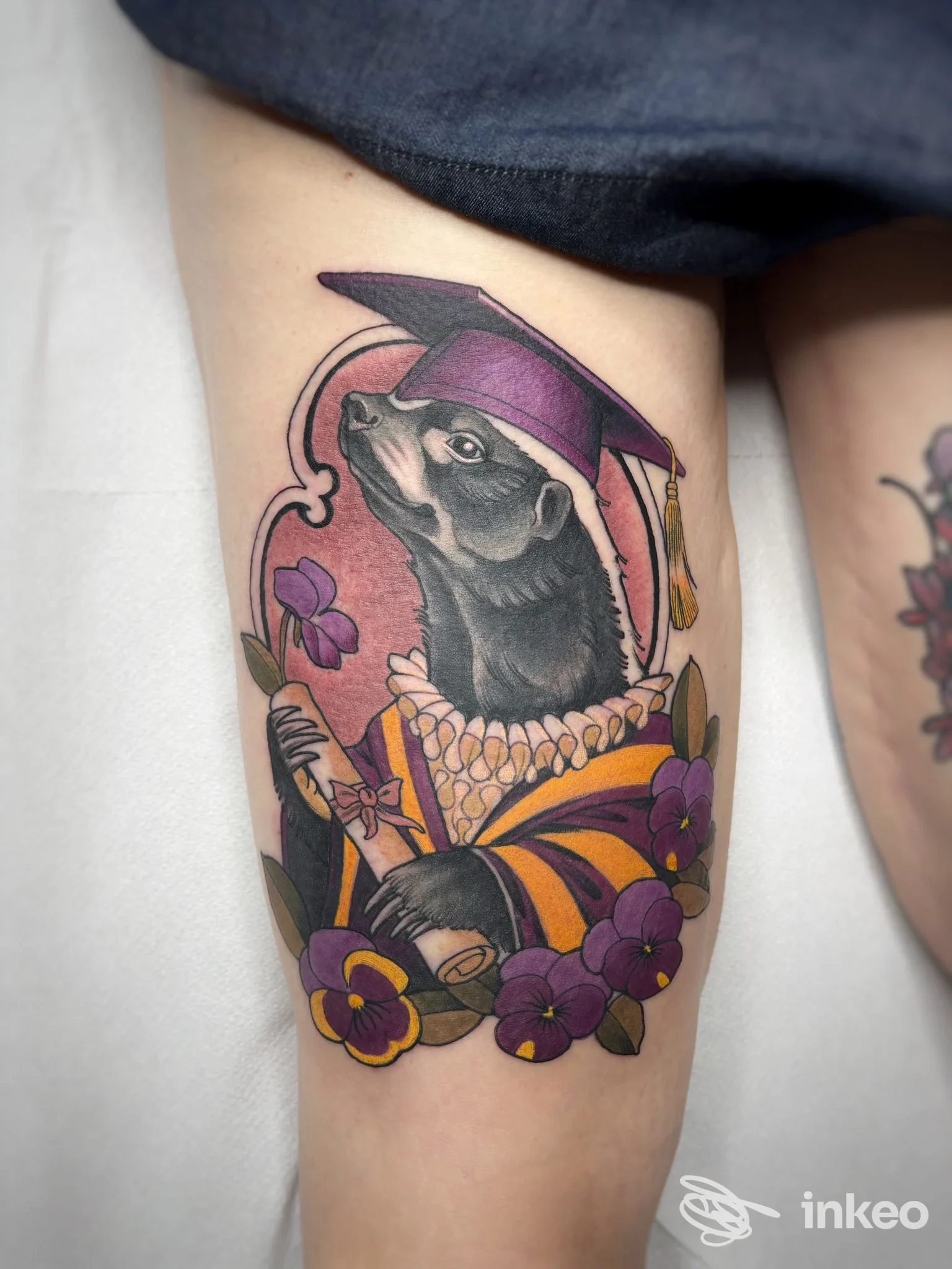 Tatuaggio neo-traditional su coscia con animale in tocco di laurea e fiori, La Montanara Tatuata, Borgo Valsugana.