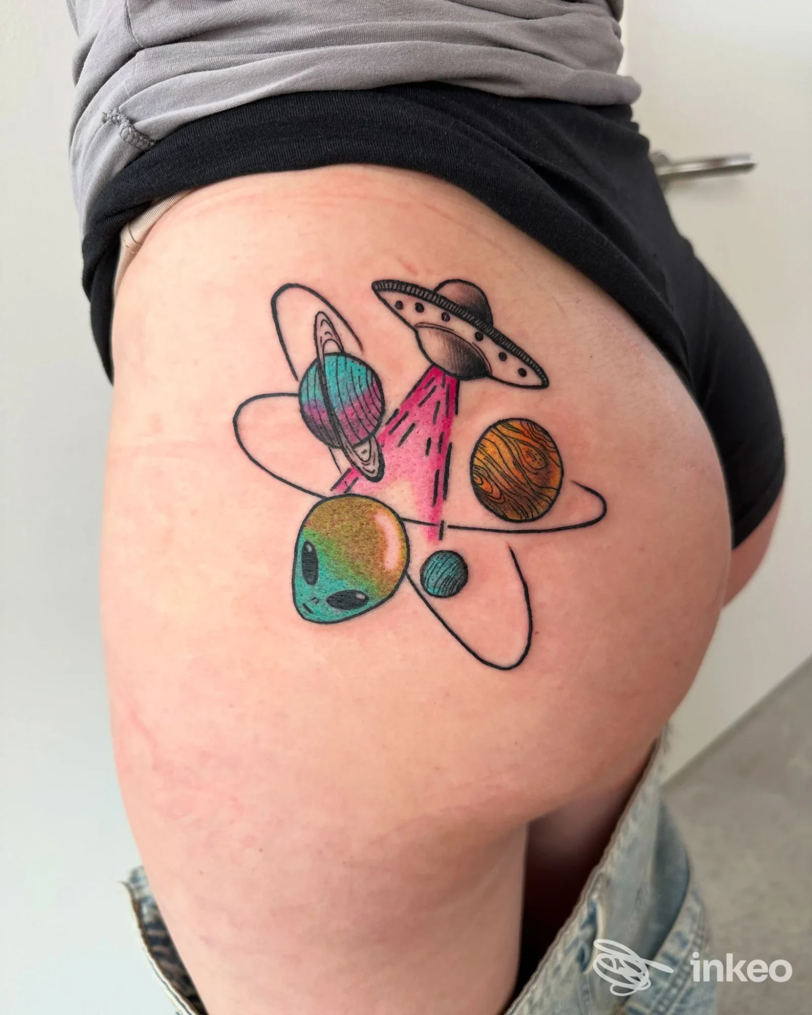Tatuaggio colorato con UFO, pianeti e piccolo volto alieno sul gluteo, realizzato da Little Ink Tattoo Studio a Rovereto.