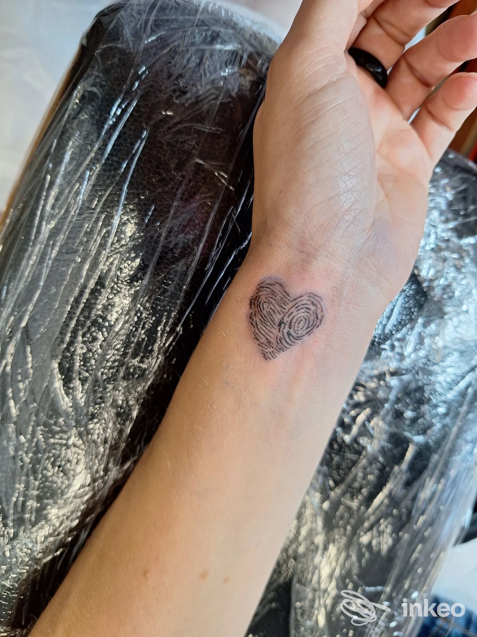 Piccolo tatuaggio a forma di cuore composto da impronte digitali sul polso di una persona, fotografato nello studio Mad Queen Tattoo a Bolzano.