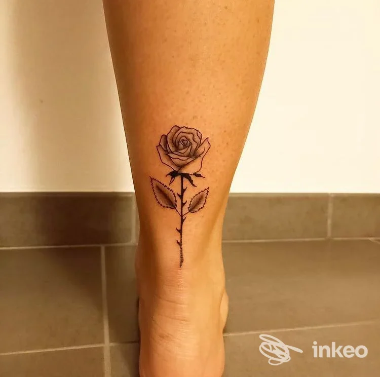 Tatuaggio a inchiostro nero di una rosa sul retro della caviglia e polpaccio, Naïf Studio Tattoo a Pinzolo.