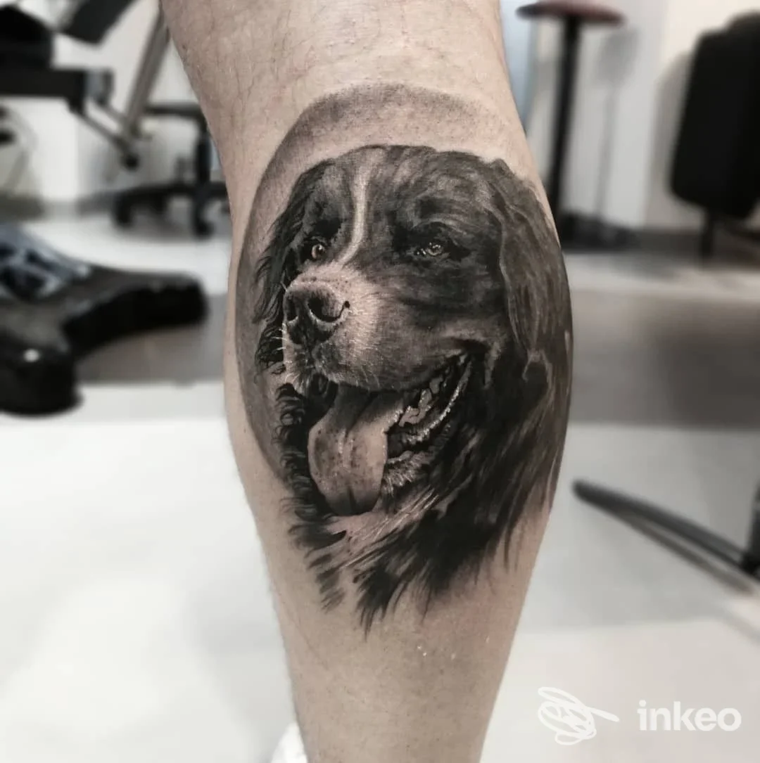 Tattoo realistico in bianco e nero di un cane sul polpaccio, eseguito sulla pelle, sfondo di studio