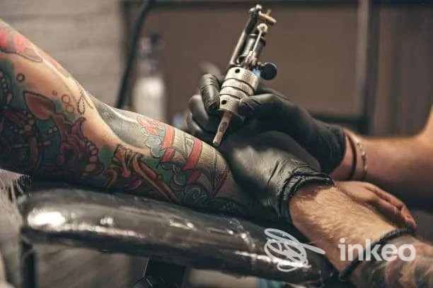 Tatuatore di Sacred Art Tattoo a Rablà al lavoro su un avambraccio colorato, dettaglio della macchinetta e degli inchiostri.