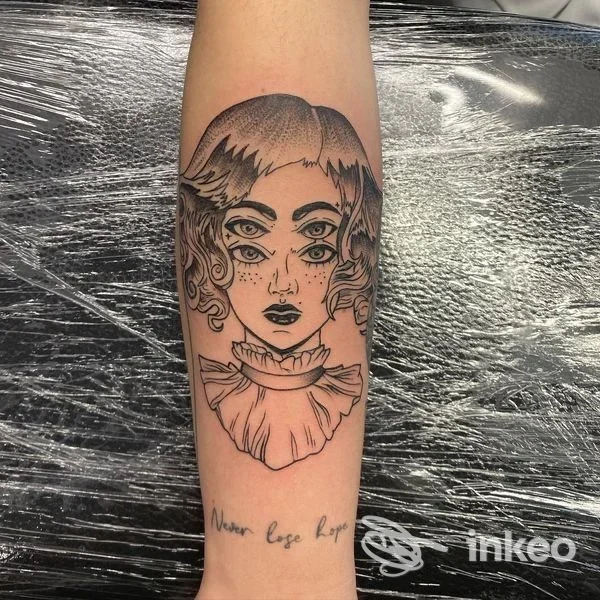 Tatuaggio in bianco e nero su avambraccio: volto stilizzato con tre occhi e colletto, foto fornita da SKY TATTOO BRUNECK a Brunico.