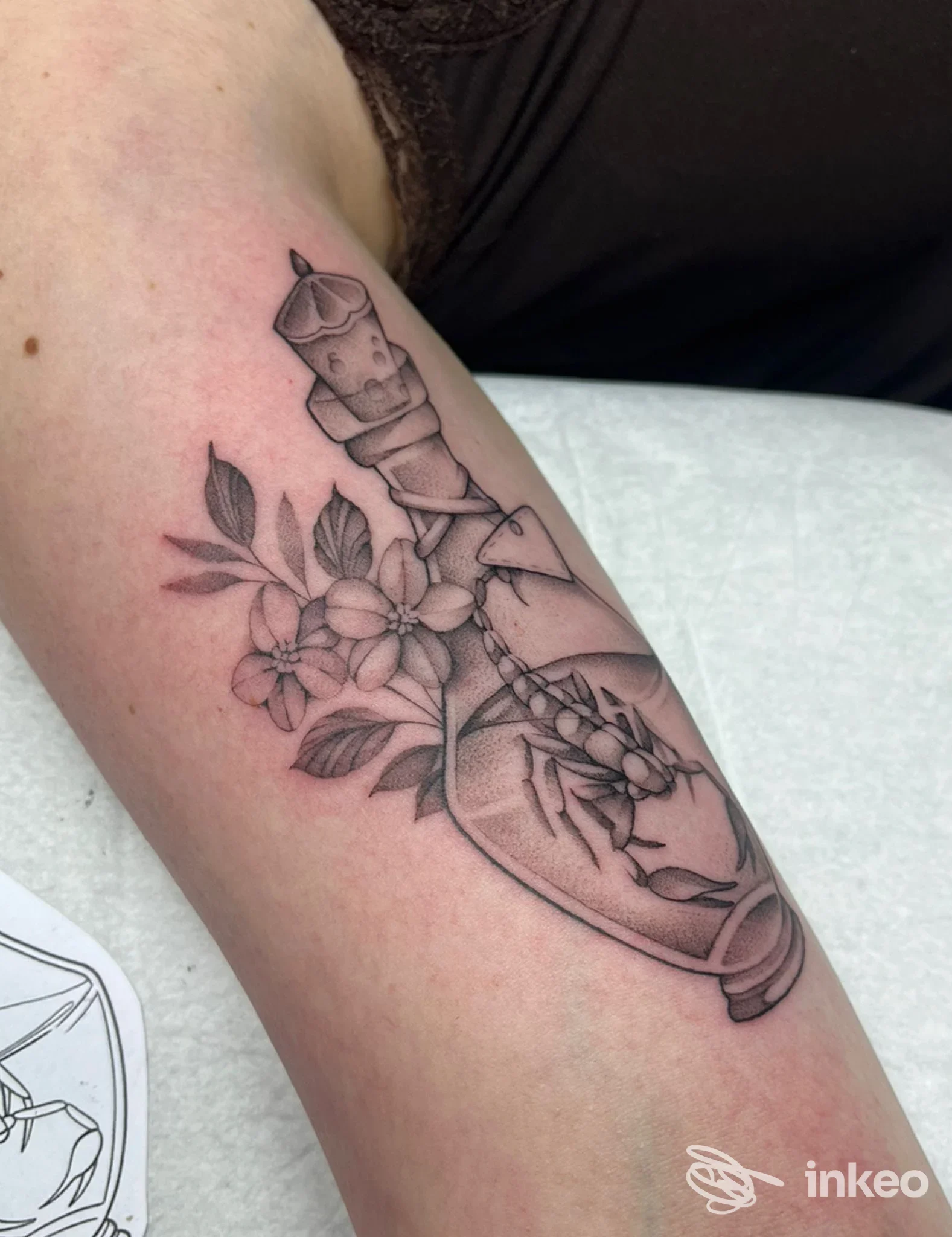 Tatuaggio in bianco e nero sull'avambraccio raffigurante una bottiglia con fiori e un ragno, realizzato da Salem Tattoo a Lana.