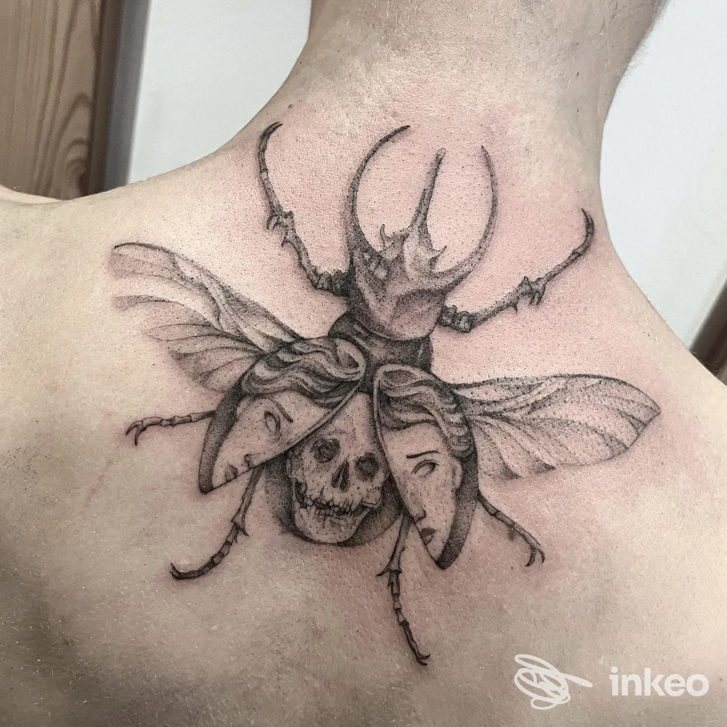 Tatuaggio in bianco e nero di un coleottero con maschere e teschio sulla parte superiore della schiena, realizzato da Salem Tattoo a Lana.