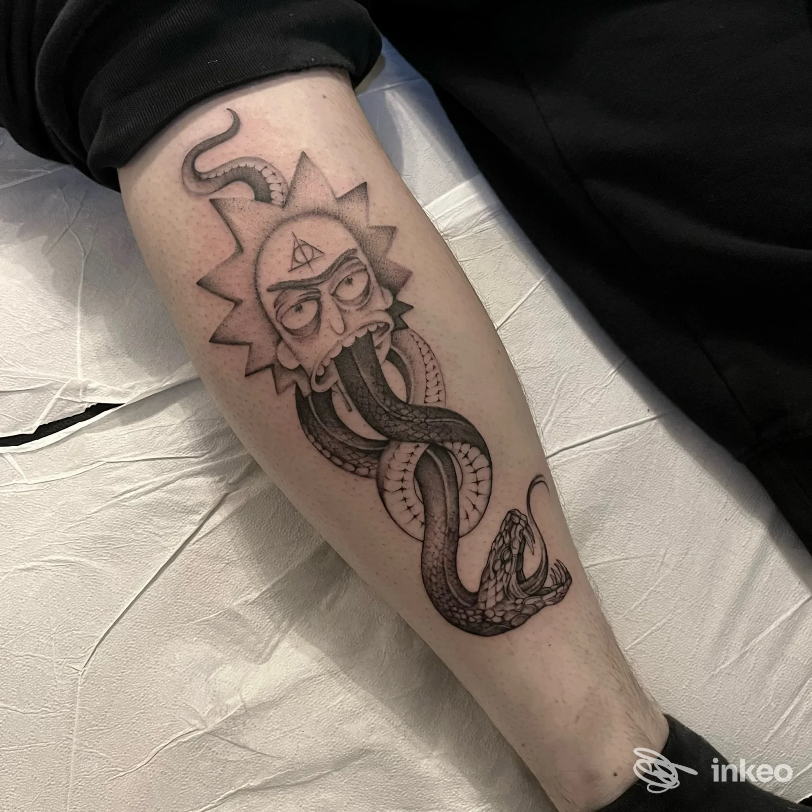 Tatuaggio in bianco e nero sull'avambraccio raffigurante un volto stilizzato da cui fuoriesce e si avvolge un lungo serpente. Salem Tattoo, Lana.