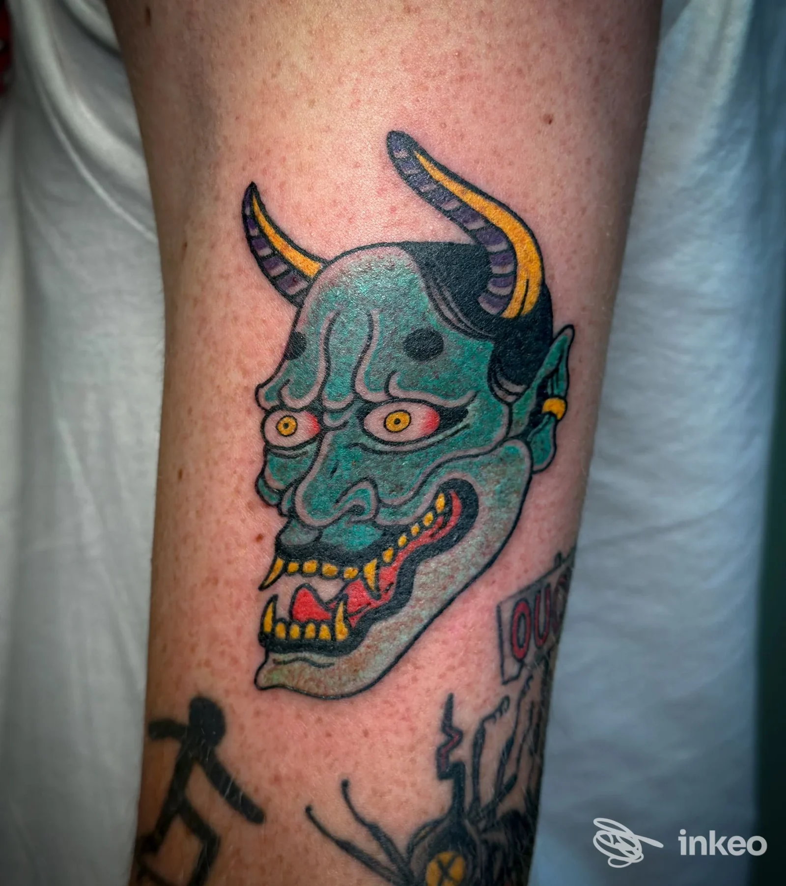 Primo piano di avambraccio con tatuaggio a colori raffigurante una maschera demoniaca; immagine fornita da SoloBuio tattoo, Rovereto.