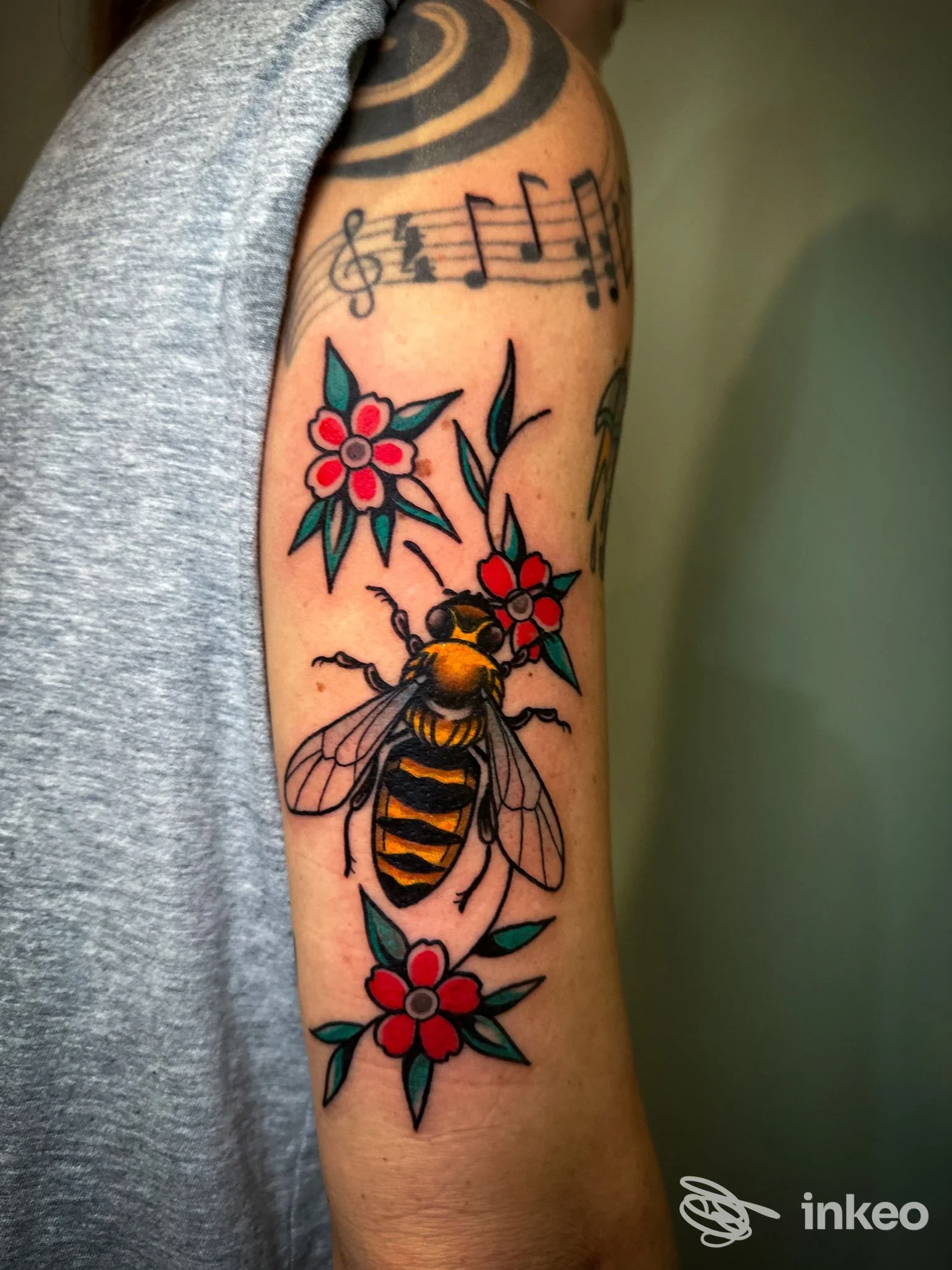 Tatuaggio tradizionale di ape e fiori sul braccio superiore, foto fornita da SoloBuio tattoo a Rovereto.