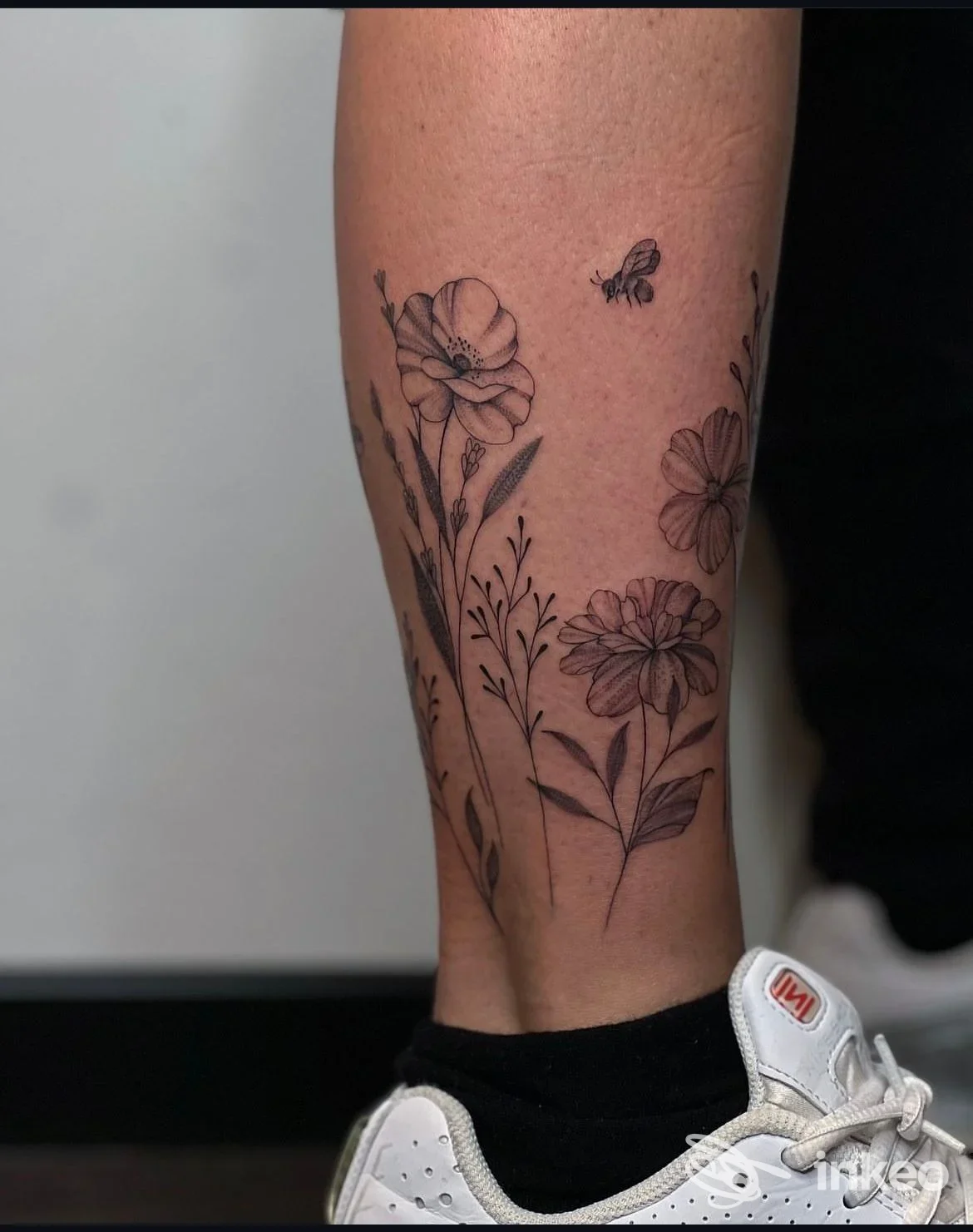 Tatuaggio floreale in nero su polpaccio, dettaglio di fiori e una piccola ape; immagine fornita dallo Studio 9 tattoo a Bolzano.