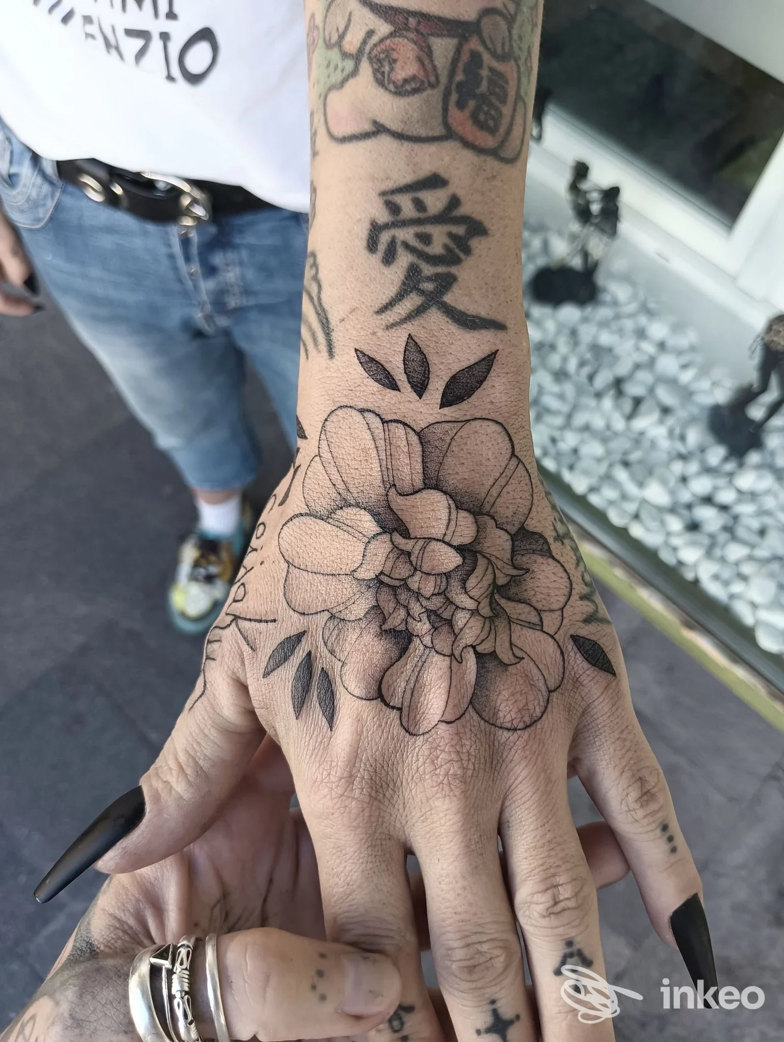 Primo piano di una mano e avambraccio tatuati con un grande fiore e carattere giapponese, foto di Oltre tattoo a Ponte Arche.
