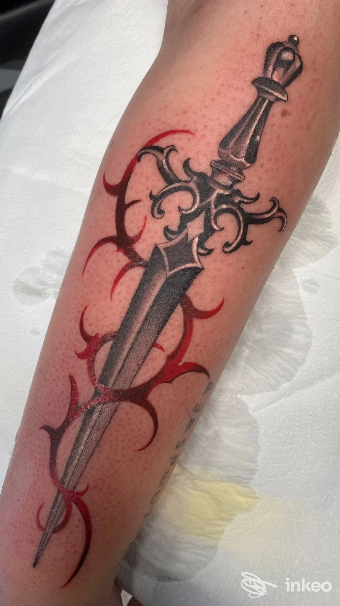 Tatuaggio su avambraccio con pugnale stilizzato e dettagli rossi, eseguito da TANUKI TATTOO SHOP, Lavis.