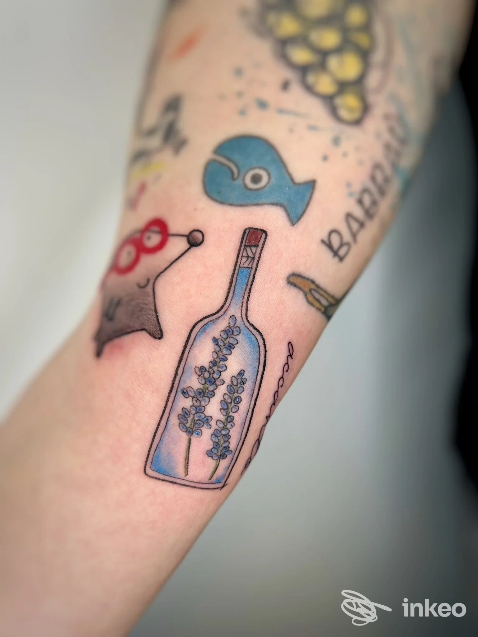 Avambraccio con piccoli tatuaggi colorati, tra cui una bottiglia con fiori; immagine fornita da TANUKI TATTOO SHOP, Lavis.