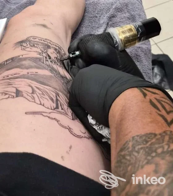 Tatuatore al lavoro su coscia con macchina per tatuaggi, foto condivisa da Tattoo NO OANS a Barbiano.