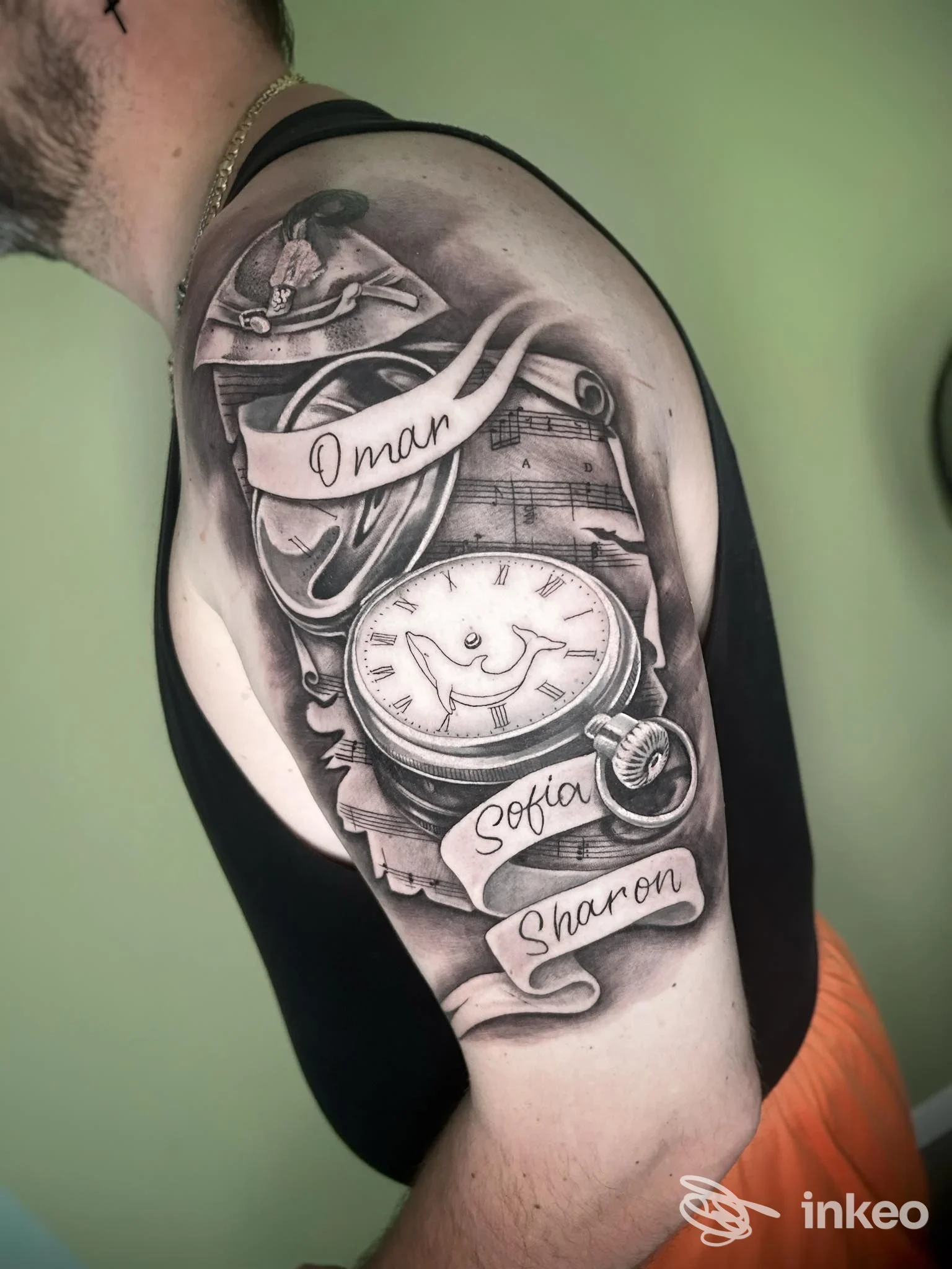 Tatuaggio black & grey su spalla e braccio con orologio da tasca e nastri nominativi, immagine fornita da Tattoo Society, Pergine Valsugana.