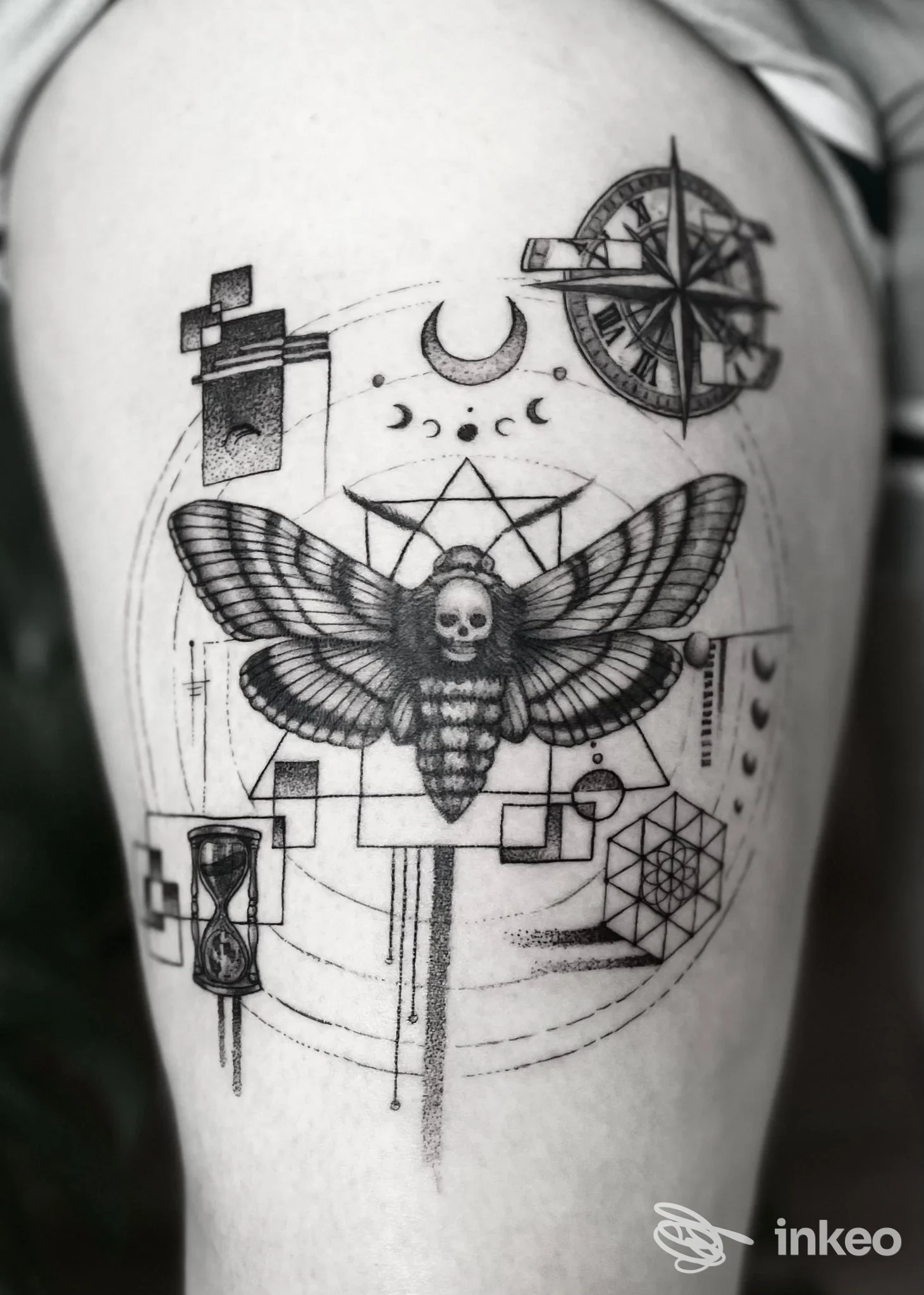 Tatuaggio su coscia: falena con teschio al centro, elementi geometrici, bussola e clessidra. Foto inviata da Tattoostube 22, Bressanone.