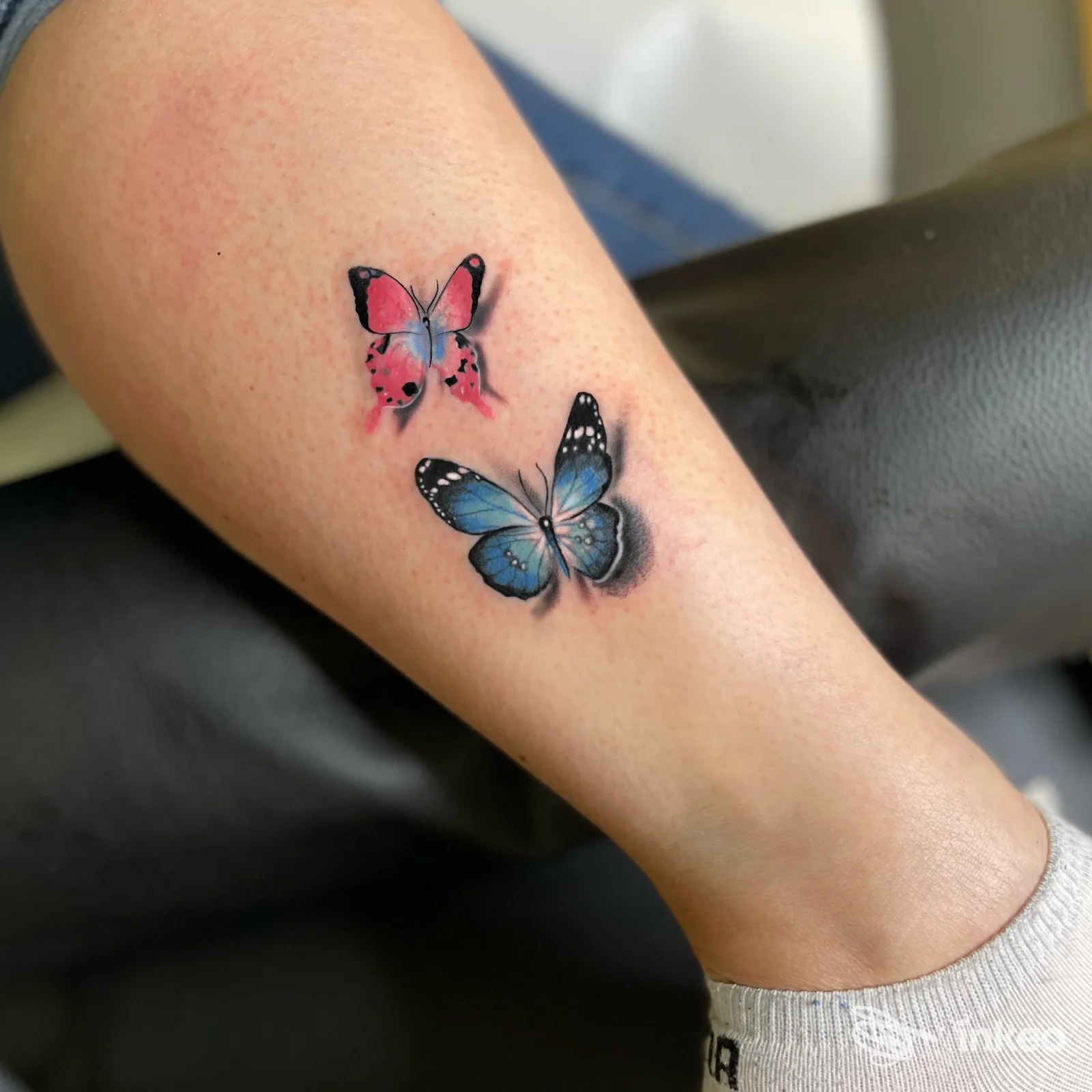 Due farfalle tatuate a colori sulla parte inferiore della gamba, lavoro di Tintanera Tatuaggi e Piercing Atelier a Pergine Valsugana.