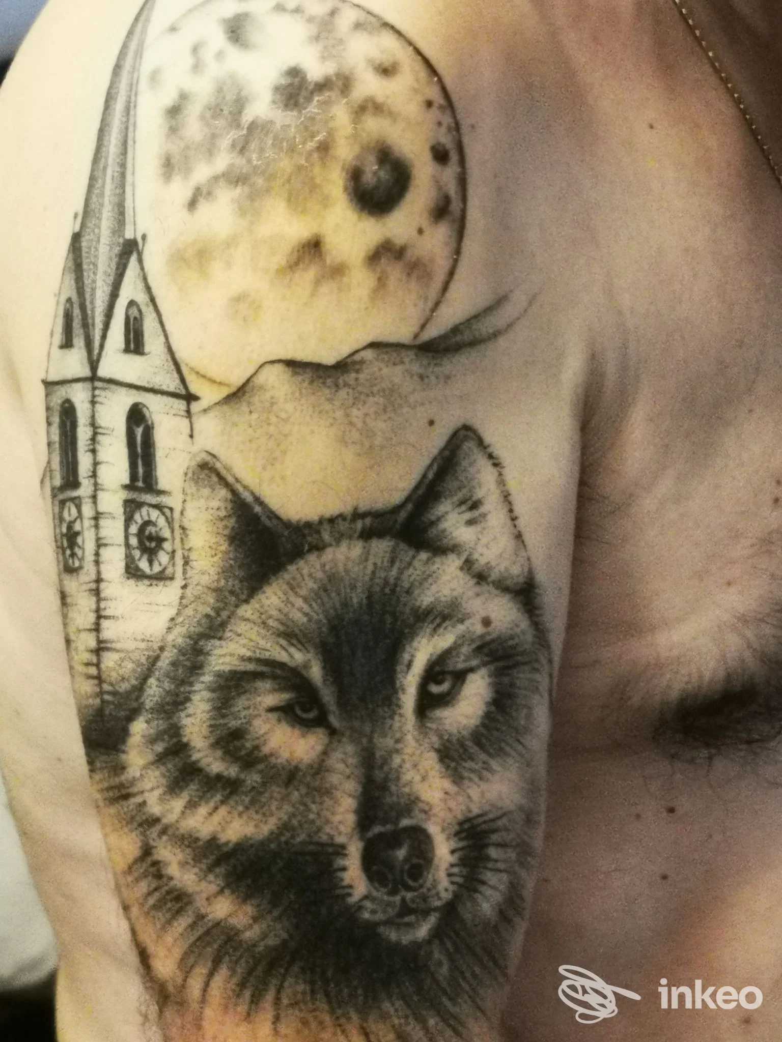 Tattoo realistico di un lupo sulla spalla sinistra con luna e una torre, realizzato direttamente sulla pelle.