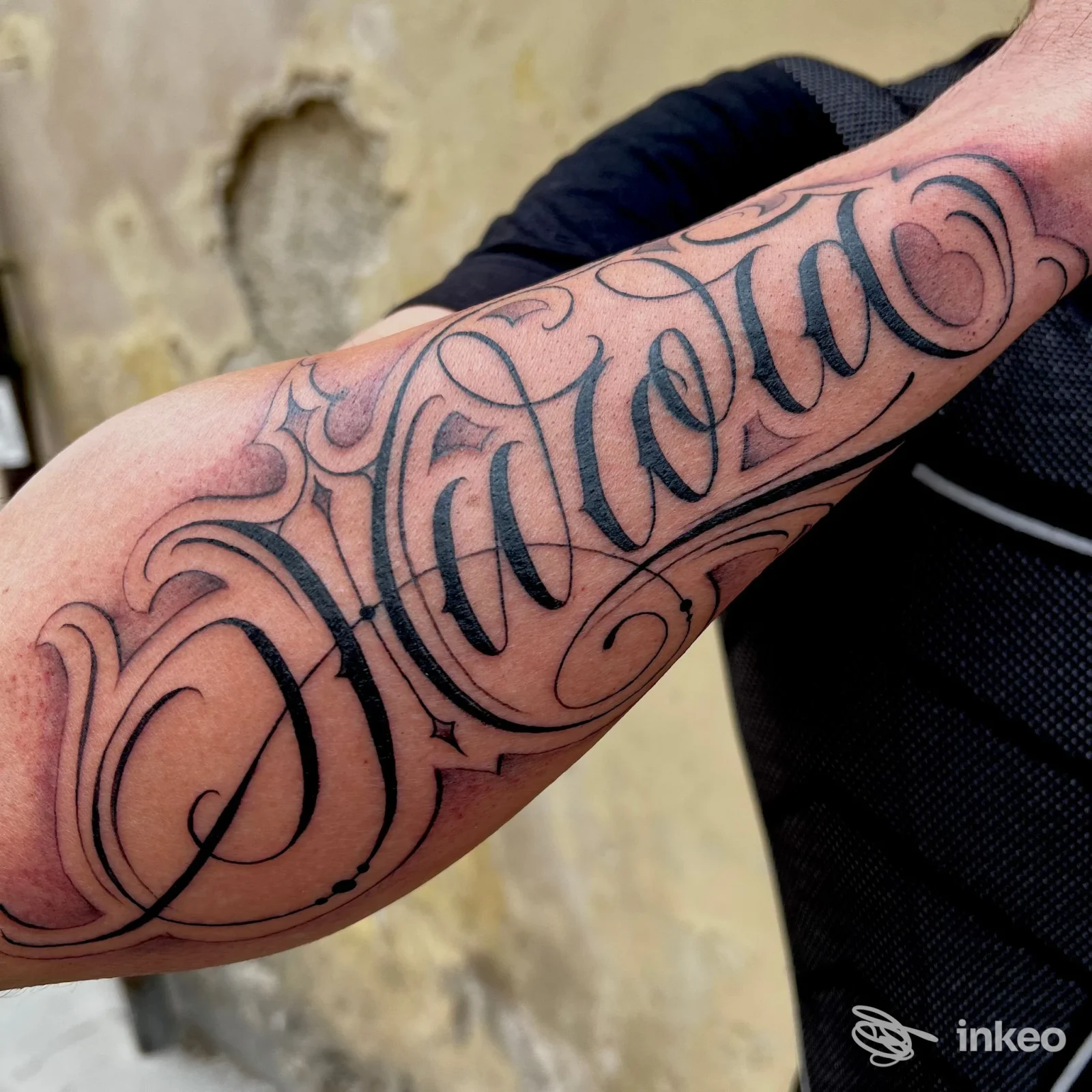 Tatuaggio calligrafico nero in primo piano sull'avambraccio, realizzato da Armink tattoo studio a Bevagna.