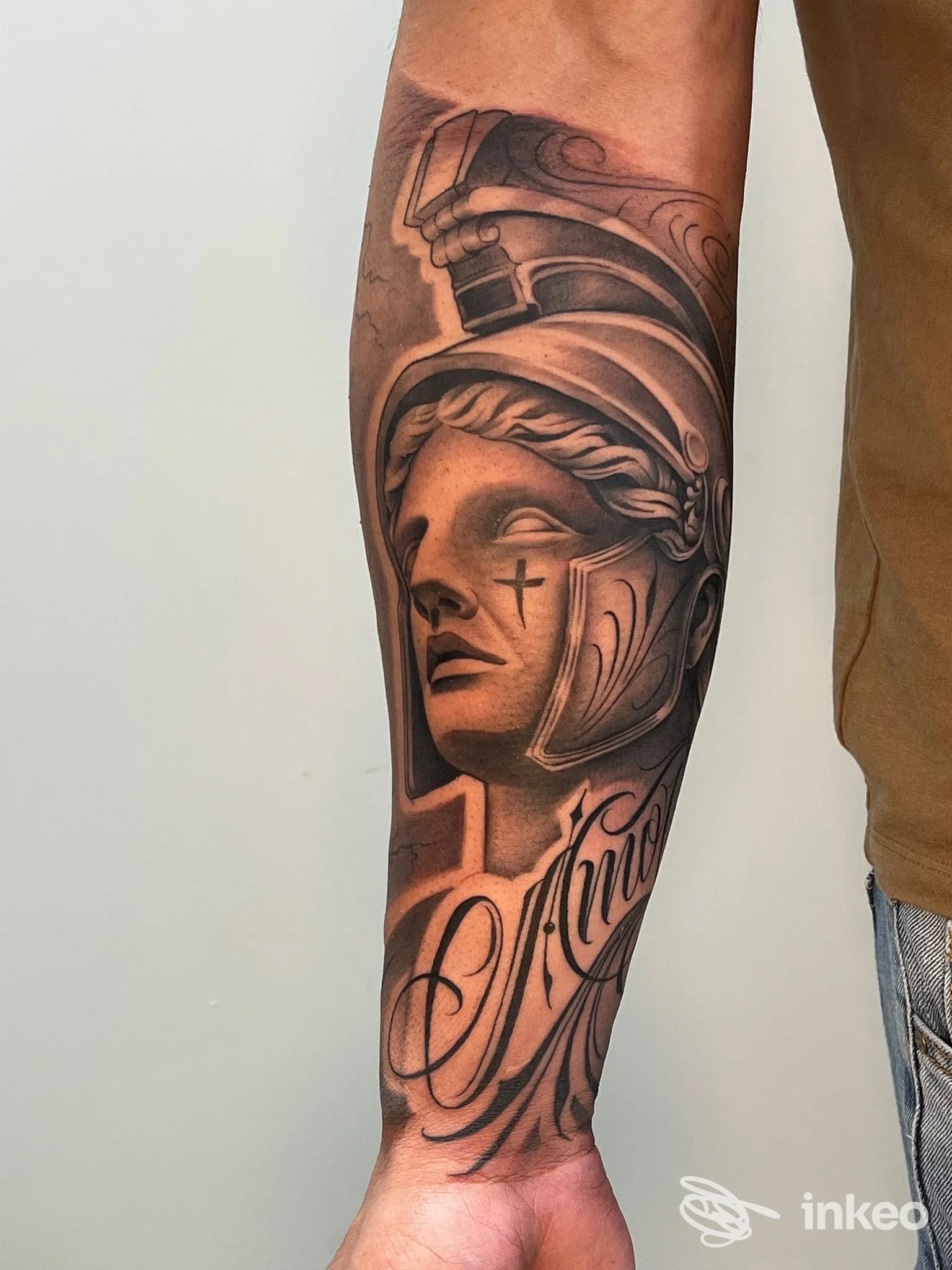 Tatuaggio realistico bianco e nero su avambraccio con figura elmifica e scritta, foto fornita da Armink tattoo studio, Bevagna.