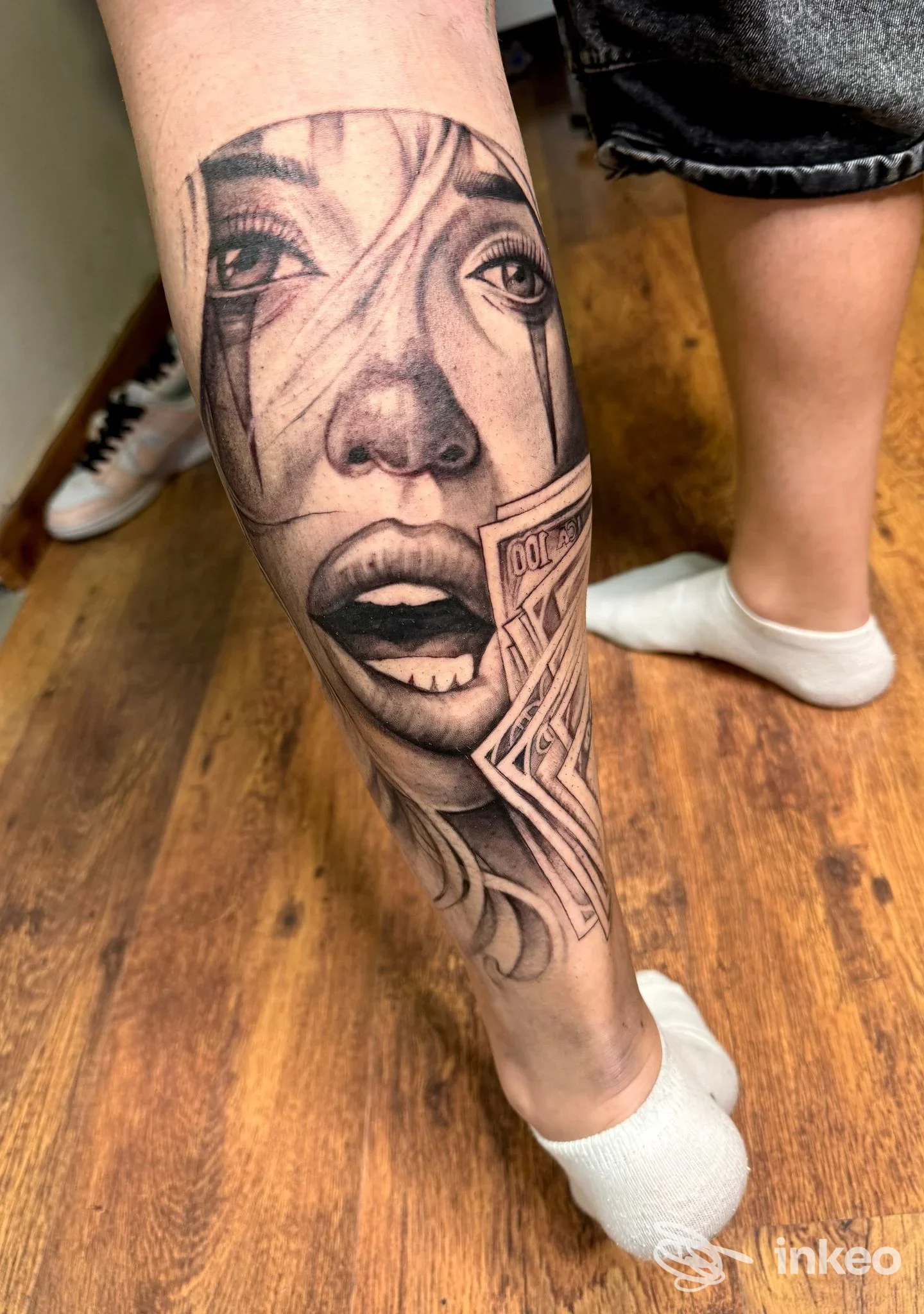 Tatuaggio realistico in bianco e nero di un volto e banconote sul polpaccio, scattato presso Atelier Tattoo Studio di Carmine Cerbone, Corciano.