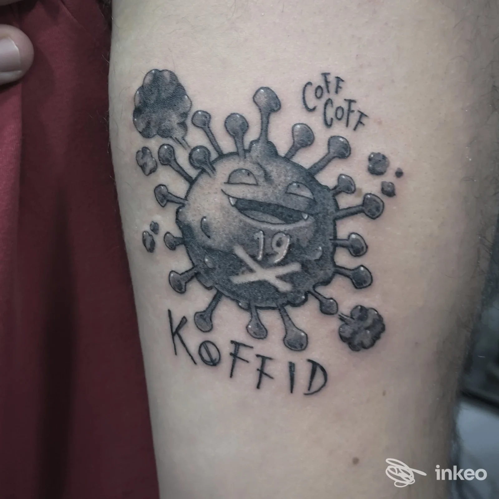 Tatuaggio bianco e nero a Città di Castello presso Caracol Tattoo: caricatura di virus con numero '19' e scritta 'KOFFID' su avambraccio.