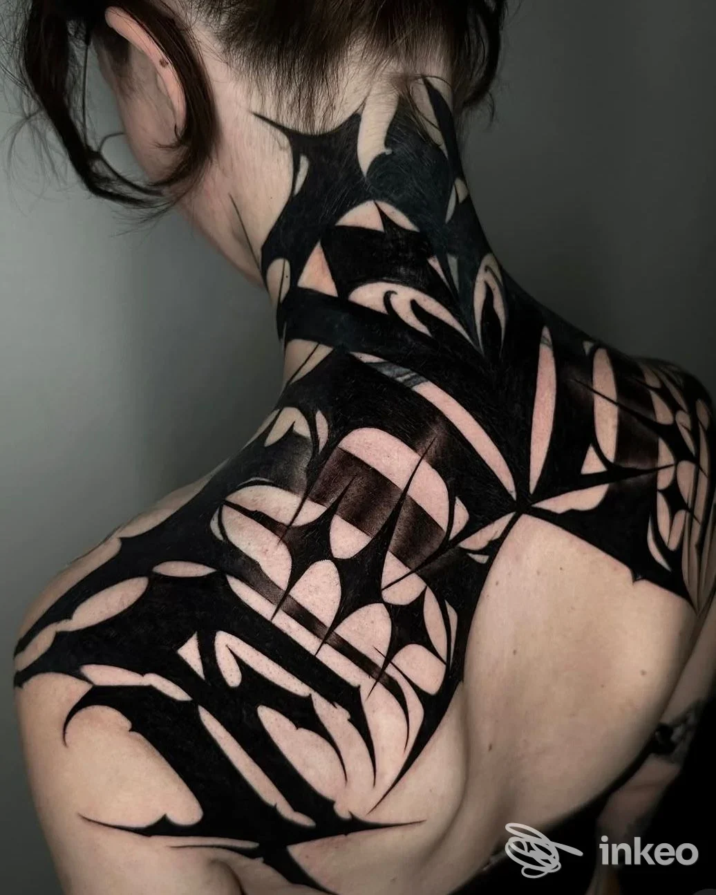 Tatuaggio corporeo visibile sul collo e sulla spalla sinistra, in stile geometrico/tribale nero, senza intero viso visibile.
